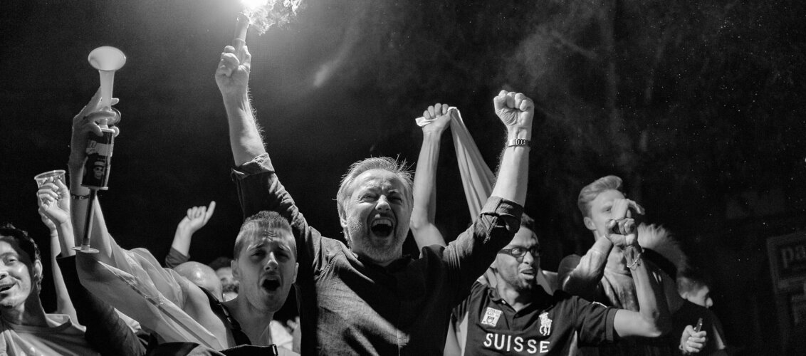 there is a crowd of jubilant football fans celebrating a victory of their team. the image is black and white. one fan is holding a flare over his head.