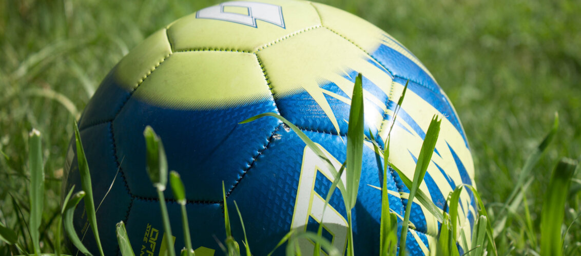 there is a soccerball yellow and blue which is lying in the grass.