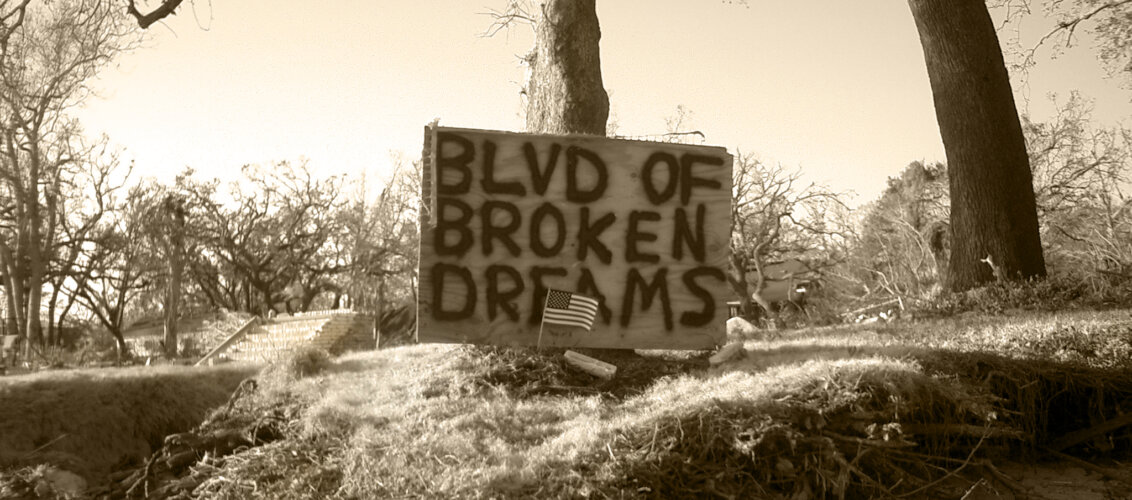 a cardboard with "Boulevard of broken dreams" written on it before a tree
